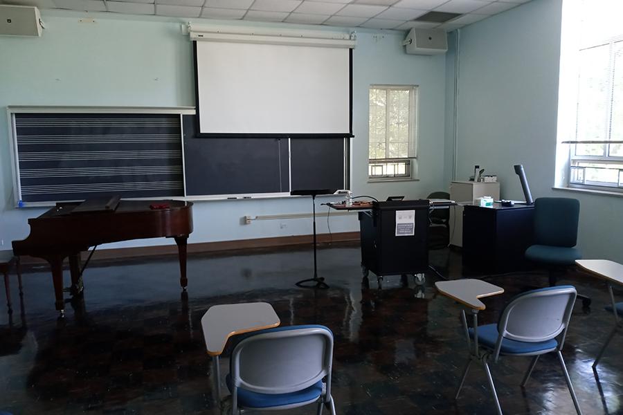 View of Presser 202 showing desks, lectern, projection screen, baby grand piano, and chalkboard with musical staff